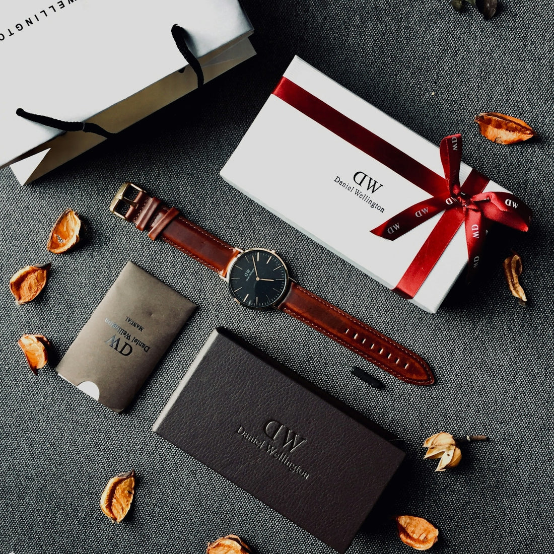 round black analog watch with brown leather stral with box and paper tote bag on gray yextile